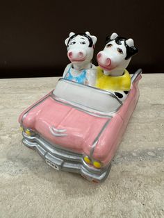 two cow figurines sitting on top of a pink car