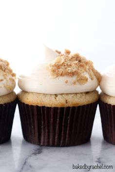 three cupcakes with white frosting and sprinkles on top are lined up