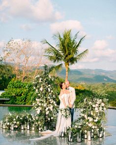 a bride and groom standing next to each other in front of a pool surrounded by greenery