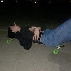 a man laying on top of a skateboard in the street at night with his hand up to his face