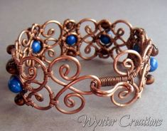 a copper wire bracelet with blue beads and filigrees on the end, sitting on a table