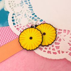 two yellow flower shaped earrings sitting on top of a pink and white lace tablecloth