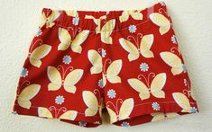 a pair of red shorts with yellow and blue butterflies on them hanging from a wall