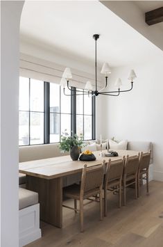 a dining room table with chairs and a bench in front of large windows that look out onto the street