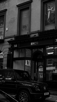 a black and white photo of a car parked in front of a building on the street