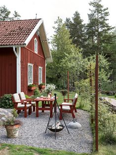 an outdoor patio with chairs and table next to a red house in the woods,