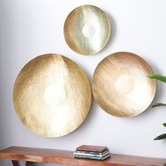 three gold plates are hanging on the wall above a wooden table with a book and plant