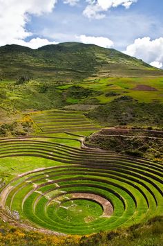 a large circular structure sitting on top of a lush green field next to a mountain