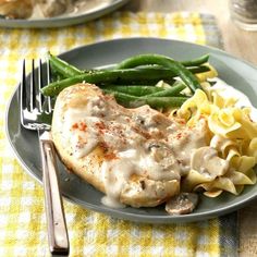 a plate topped with chicken, pasta and green beans next to a fork on a checkered table cloth