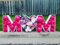 the word mom spelled out in front of a fence with balloons and flowers on it