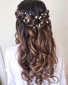 the back of a woman's head with long wavy hair and flowers in her hair