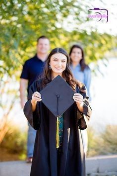 a woman in a graduation cap and gown holding up a black hat with her family behind her