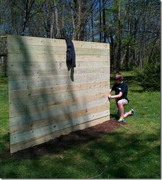 a young boy sitting on top of a wooden bench next to a wall in the grass