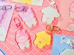 some cute little animal shaped key chains on a pink table with paper clips and tags