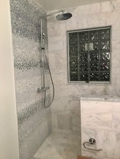 a bathroom with marble walls and flooring next to a walk in shower, glass block window