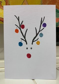 a handmade christmas card with a reindeer's head and balls hanging from its antlers