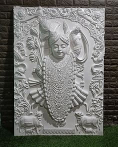 an intricately carved white wall hanging on the side of a brick building with green grass in front of it