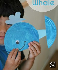 a young boy holding up a paper plate shaped like a fish with the word whale on it