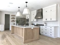 a large kitchen with white cabinets and wooden flooring, two pendant lights hanging over the island