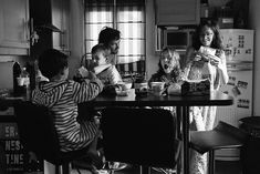 a group of people sitting around a kitchen table eating food and drinking water from cups