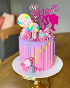 a pink and purple birthday cake with candy decorations on top, sitting on a table