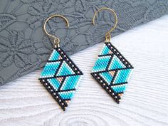 a pair of blue and black beaded earrings sitting on top of a piece of fabric