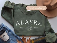 Embrace the spirit of the Last Frontier with our meticulously embroidered Alaska sweatshirt, a cozy tribute to the wild and beautiful North. Stay warm and show your love for Alaska in style with this must-have addition to your wardrobe. ✨DESCRIPTION✨  🌟GILDAN 18000 Unisex Sweatshirt - Embroidered design *100% cotton (Sport Grey is 90% cotton, 10% polyester; Ash Grey is 99% cotton, 1% polyester, heather colors are 50% cotton, 50% polyester. *Sweatshirts are in UNISEX sizing. Select your usual size for a more fitted look, or size up for a more relaxed fit. *Please note that the embroidery design has a backing on the inside of the sweatshirt to support the fabric and stitches. *Fabric Weight 5.0-5.3 oz/yd² (170-180 g/m²) *pre-shrunk jersey knit, air jet spun yarn for a soft feel & reduced pi Alaska Sweatshirt, Alaska Moose, Elizabeth Bennet, Family Cruise, Alaska Cruise, Womens Sweater, Sweater Gift, Pride And Prejudice, Cozy Sweatshirts