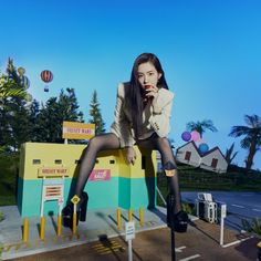 a woman sitting on top of a yellow and blue box with balloons flying in the background