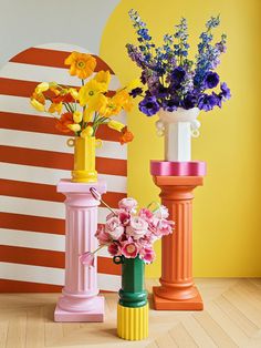 three different colored vases with flowers in them on a wooden floor next to an orange and white striped wall