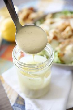 a spoon full of dressing being held over a salad in a mason jar on a table