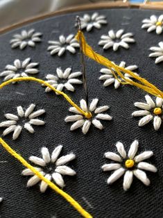 some white and yellow flowers are being sewn together on a black piece of fabric