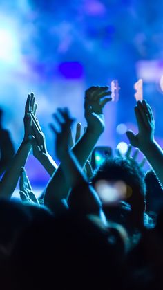 many people are raising their hands up in the air at a concert with bright lights