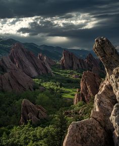 the landscape is full of large rocks and green trees, under a dark cloudy sky