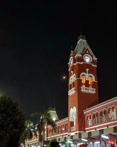 the clock tower is lit up at night in front of people walking on the sidewalk