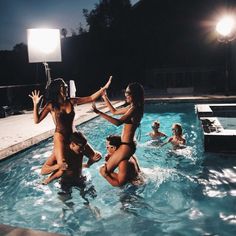 several women in a pool playing with each other and some lights on the wall behind them