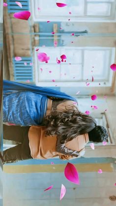 a woman laying on top of a bed covered in pink petals next to a window