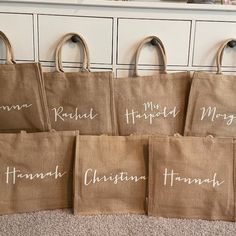 six bags with names are lined up on the floor in front of a white dresser