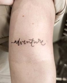 the word adventure written in cursive font on someone's arm with a small tattoo