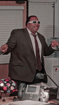 a man in a suit and tie with sunglasses on his face standing next to a desk