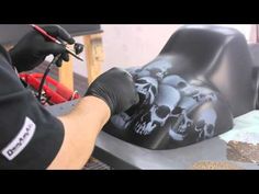 a man in black shirt and gloves working on a skull head sculpture with tools next to it