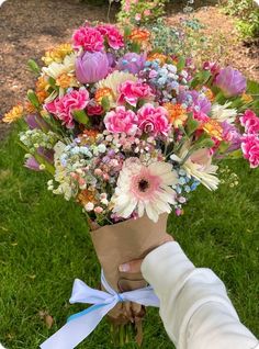 a person holding a bouquet of flowers in their hand on the grass with trees in the background