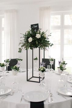 the table is set with white flowers and greenery in black vases, along with silverware