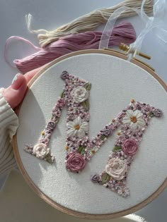 a hand embroidered letter m with flowers on it next to some yarn and thread in the background