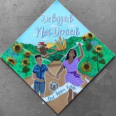 a decorated graduation cap with two people dancing in front of a field of sunflowers