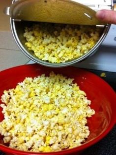 a red bowl filled with popcorn on top of a stove next to a pan full of popcorn