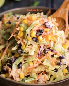 a bowl filled with coleslaw, corn and carrots next to a wooden spoon