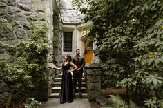 a man and woman standing in front of a stone building with stairs leading up to the door