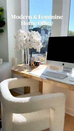 a desk with a computer and flowers in a vase on it, next to a window