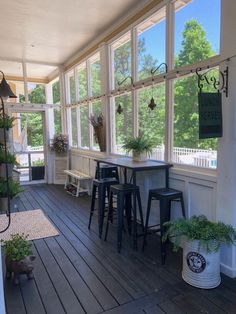 an enclosed porch with tables and stools on the floor, surrounded by potted plants