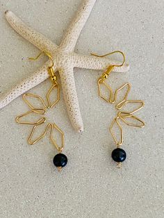 a pair of gold earrings with black beads hanging from them next to a starfish